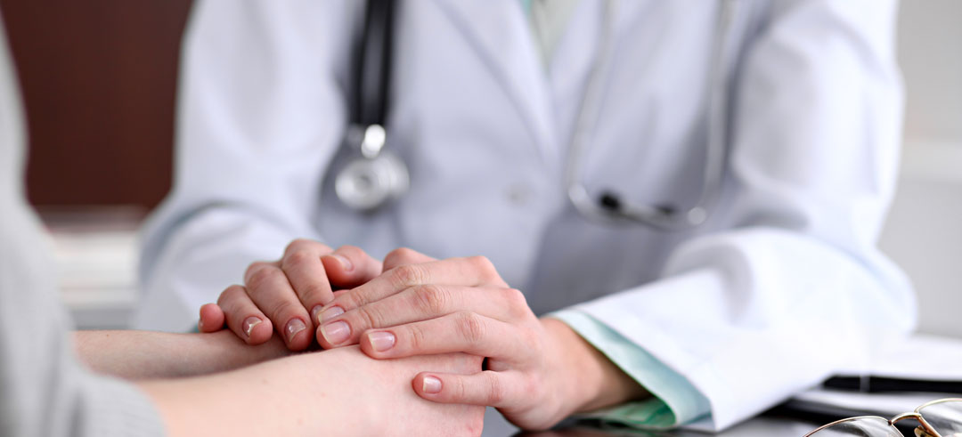 Médico sosteniendo las manos de un paciente, mostrando apoyo y compasión