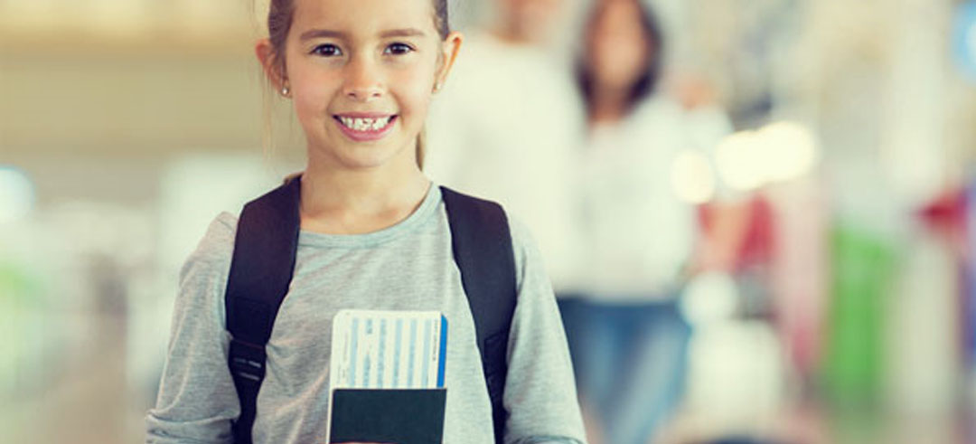 Niña pequeña sonriendo con mochila y el pasaporte de la mano